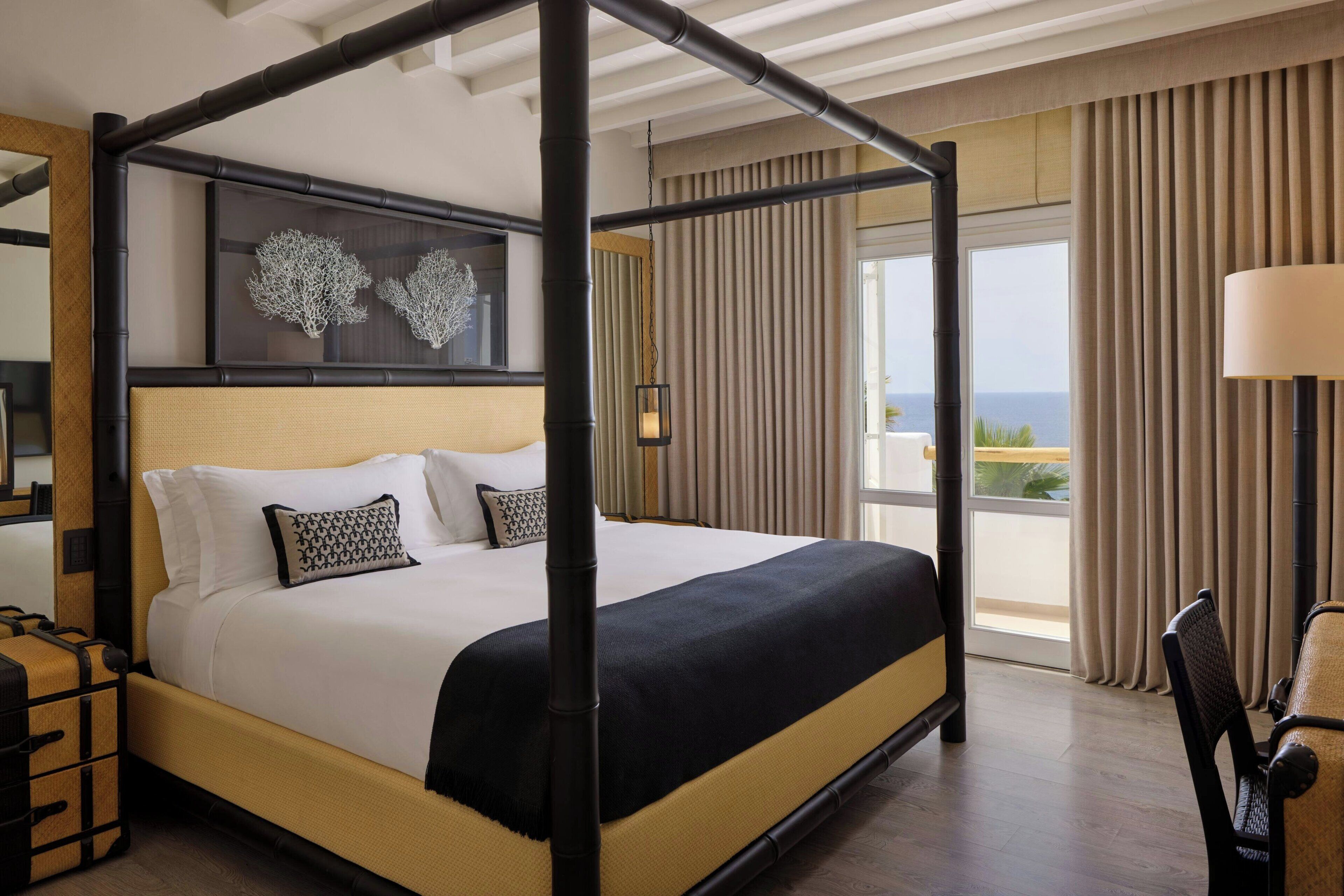 A four-poster bed with a canopy, a large window with curtains, and a view of the ocean.