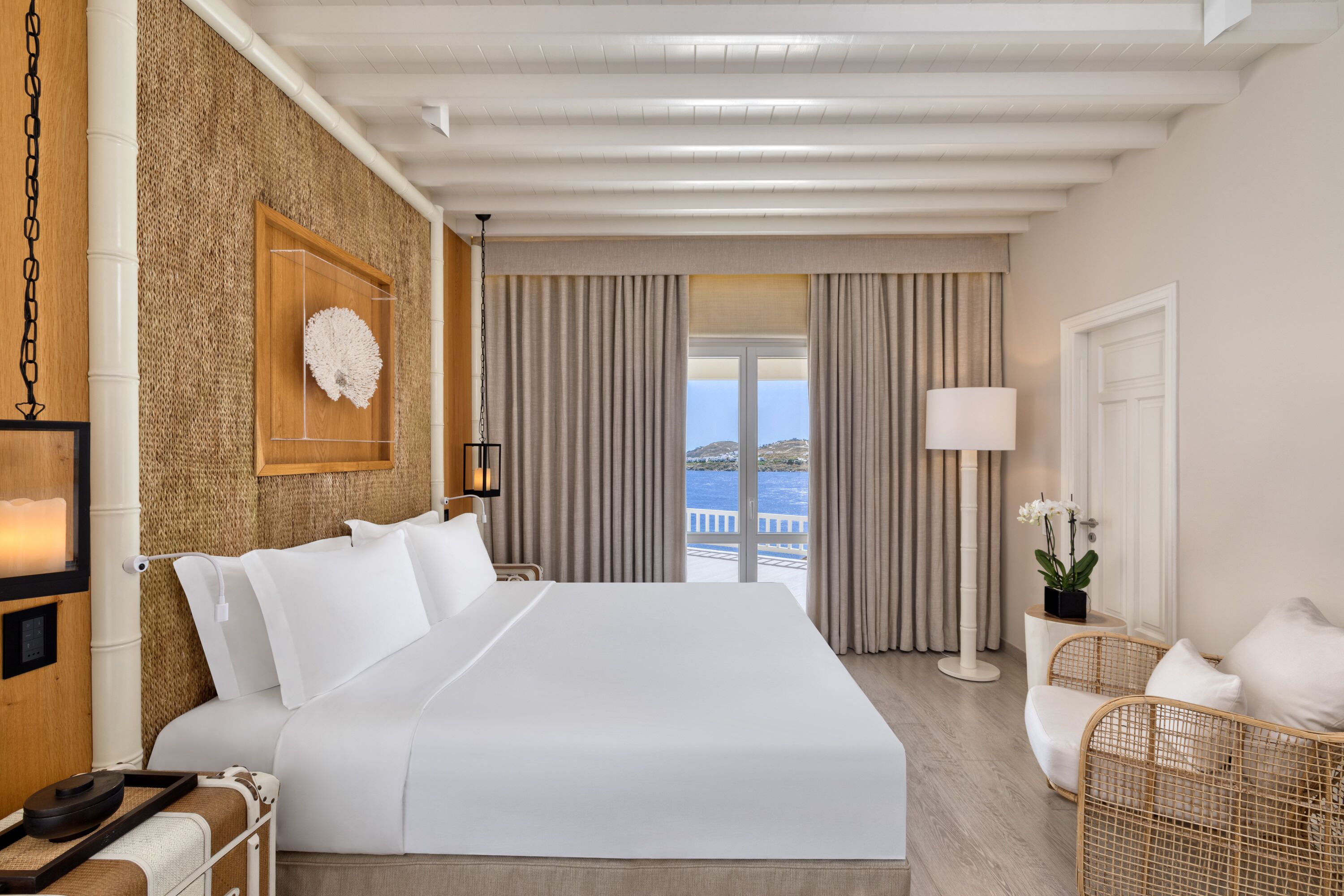 Habitación de hotel con una cama grande, vista al mar, pared de madera y balcón con cortinas.