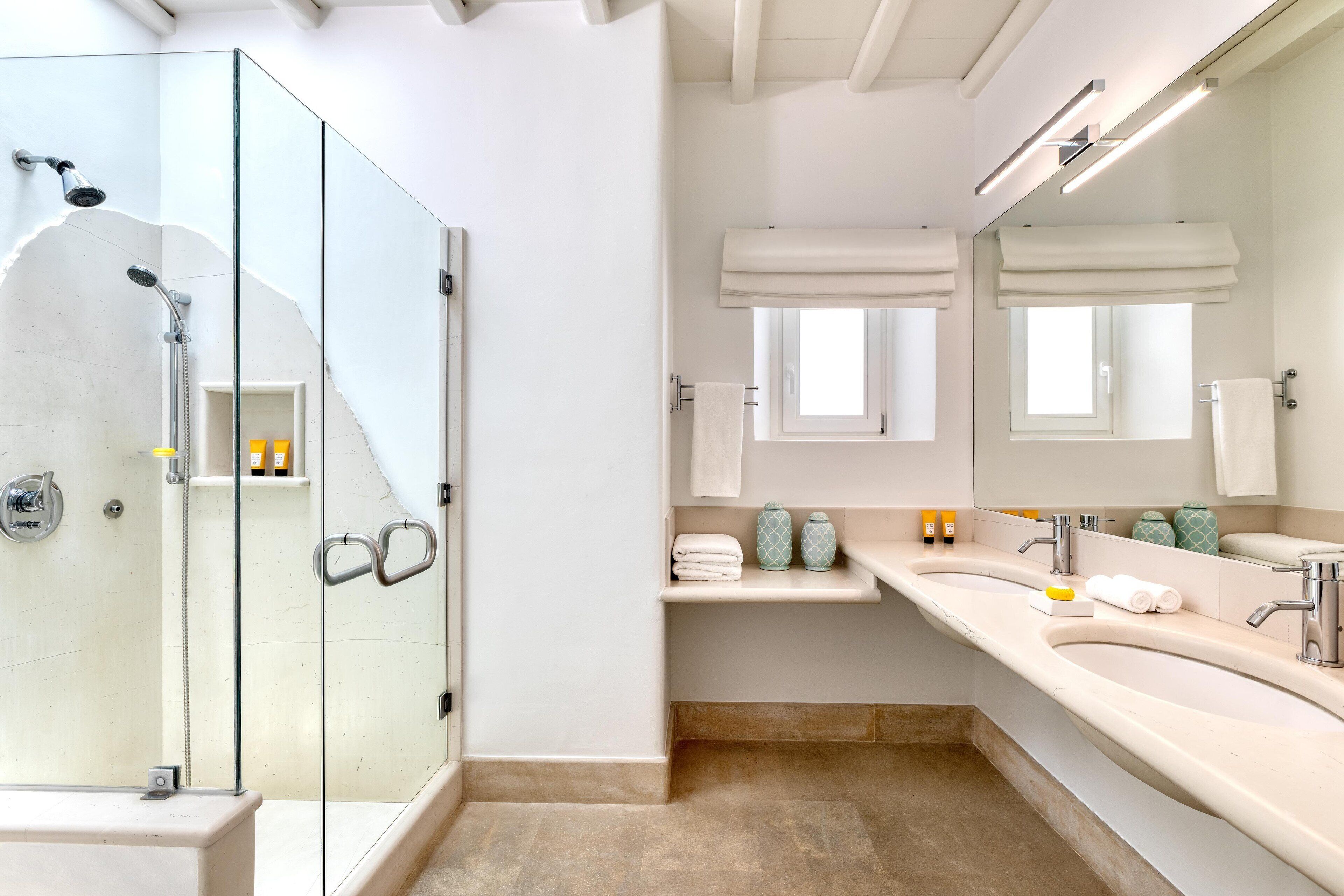 A modern bathroom with a glass-enclosed shower, a large vanity with two sinks, and a mirror above the sink.
