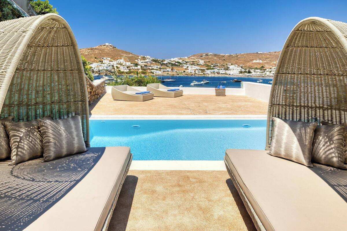 A pool area with wicker lounge chairs and a view of a coastal town.