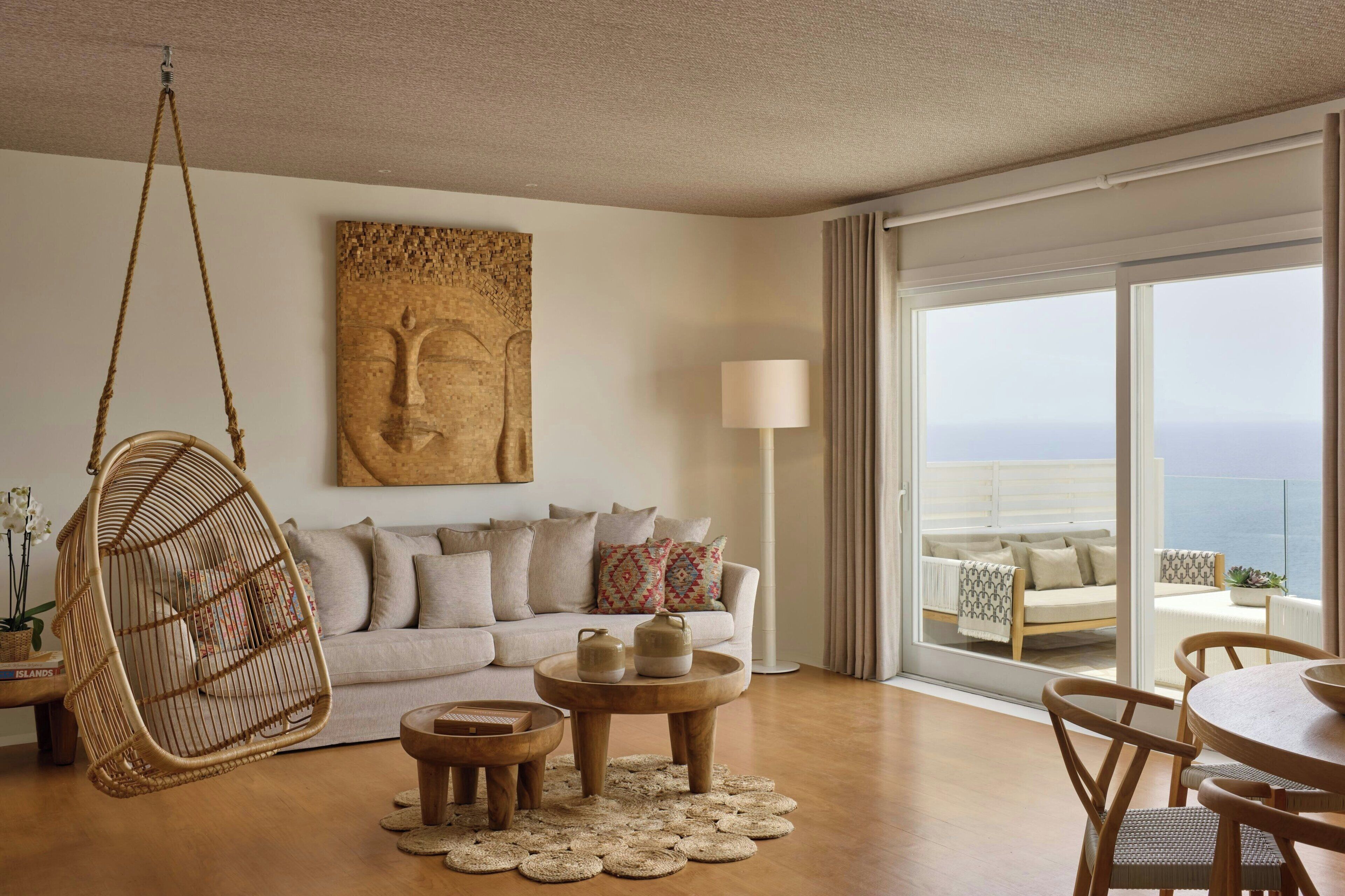 A living room with a hanging chair, a sofa, a coffee table, and a view of the ocean through large windows.