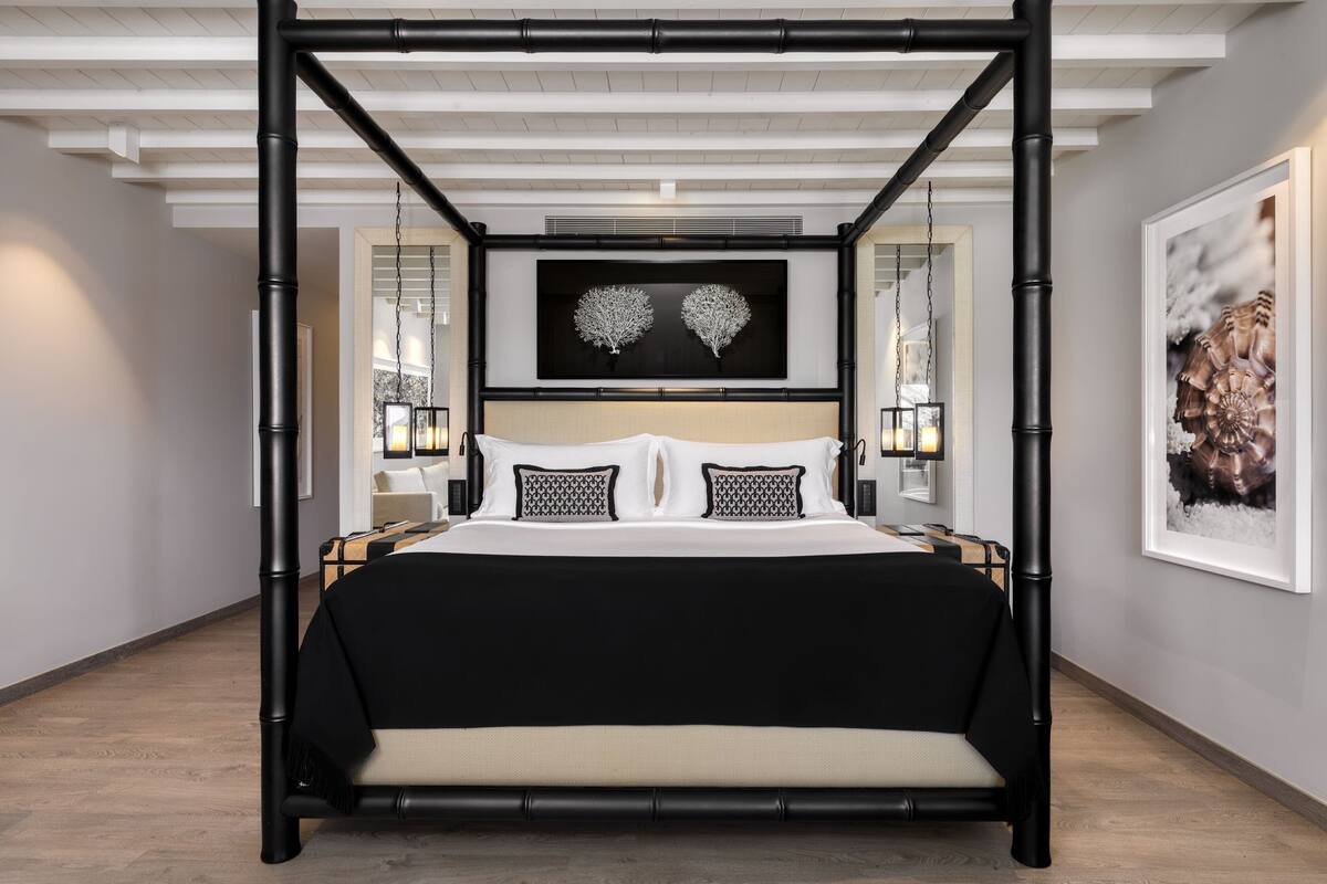 A modern bedroom with a four-poster bed, a large framed artwork above the bed, and a framed picture on the wall.