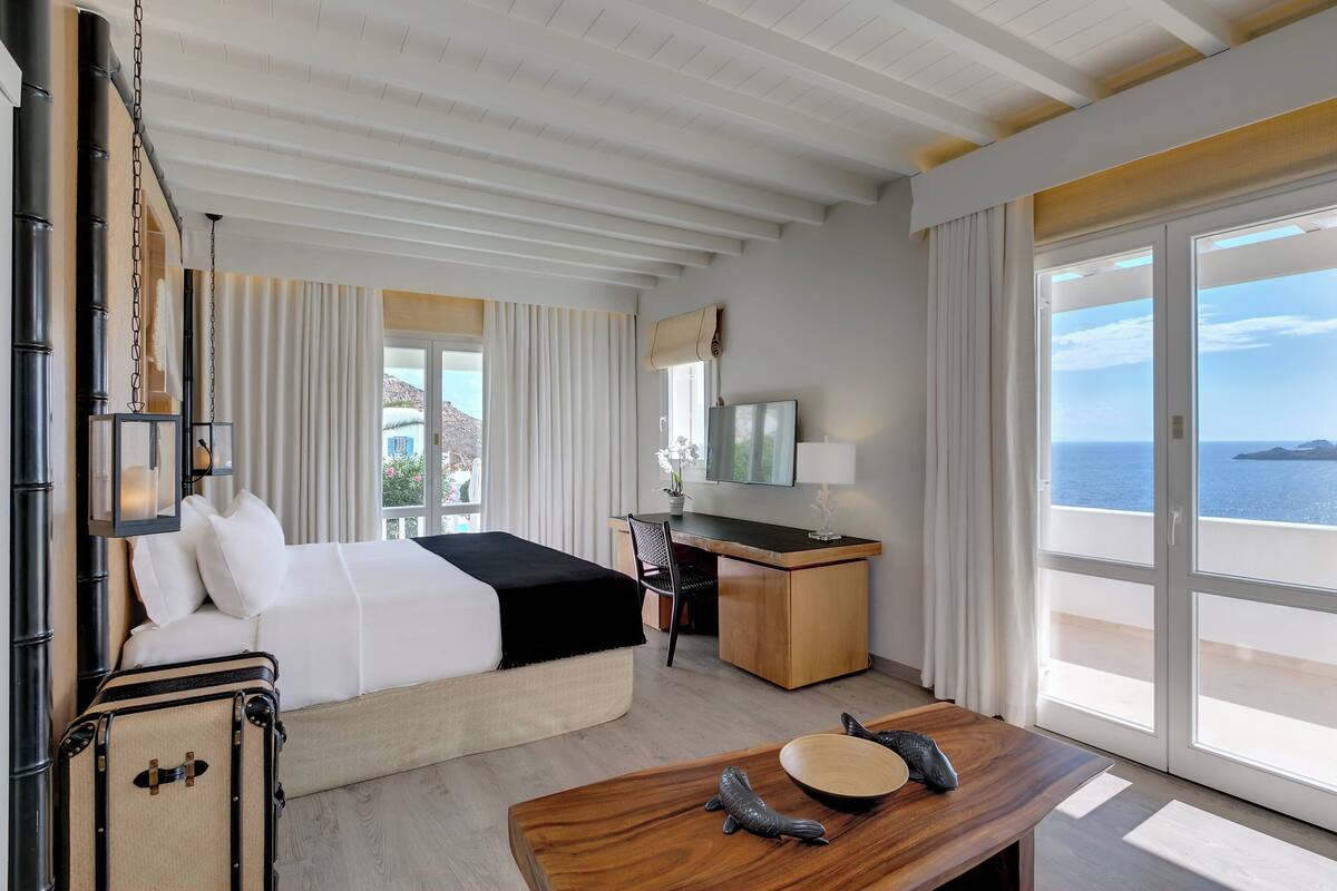A hotel room with a bed, desk, and a view of the sea.