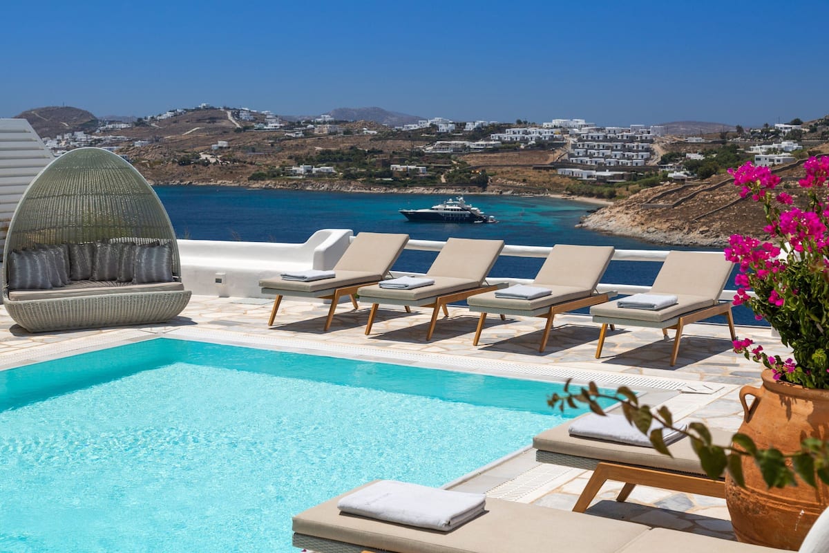 A poolside area with lounge chairs and a view of the sea and buildings in the background.