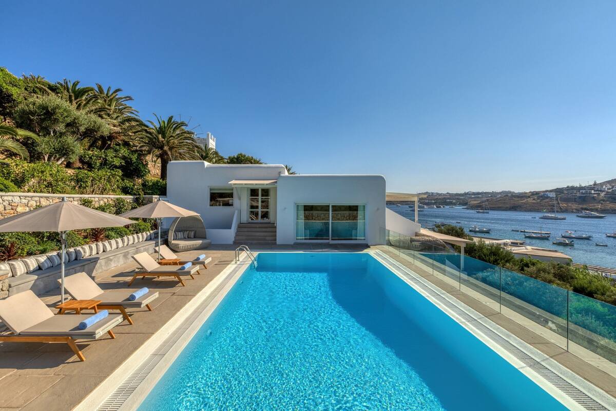 A modern pool area with lounge chairs and a glass-enclosed pool overlooking the sea.