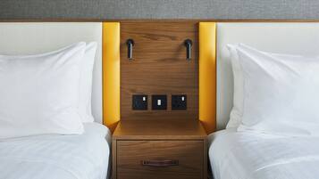 Habitación de hotel con cabecera de madera, dos almohadas blancas, mesita de noche de madera con un cajón y pared con textura.
