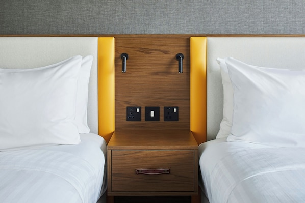 A hotel room with a wooden headboard, two white pillows, a wooden nightstand with a drawer, and a textured wall. - Cardiff Marriott Hotel (Cardiff)