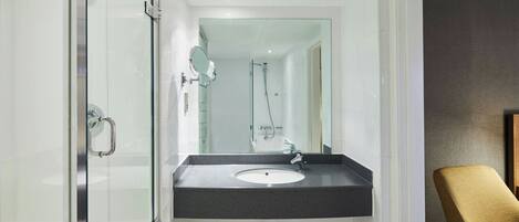 Un baño moderno con cabina de ducha de vidrio, un lavamanos con encimera oscura y una silla en la esquina.