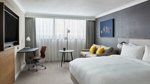 A hotel room with a bed, a desk, a chair, a TV, and a window with curtains.