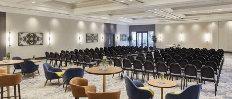 A conference room with rows of chairs, round tables with chairs, and a carpeted floor.