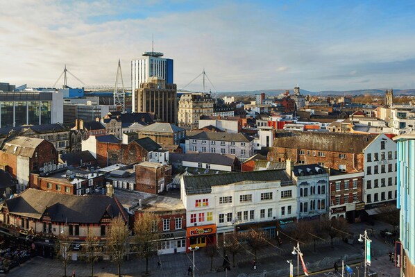 A cityscape with a mix of historical and modern buildings, including a prominent clock tower and a large cylindrical structure.