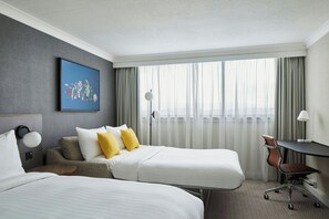 A hotel room with two beds, a desk, a chair, and a painting on the wall.