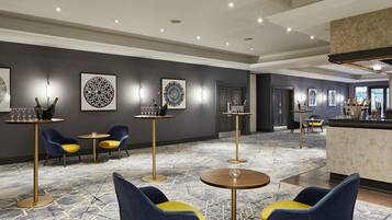 Rebedor d'hotel amb taules rodones, cadires blaves i grogues, i obra d'art penjada a la paret.