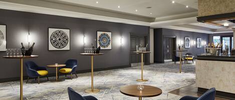 A hotel lobby with round tables, blue and yellow chairs, and wall-mounted artwork.