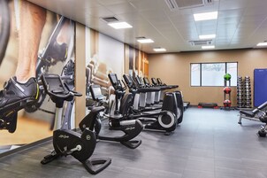 A gym with multiple cardio machines, weightlifting equipment, and a large mural on the wall.