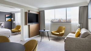A hotel room with a bed, a sofa, two armchairs, a TV, and a city view. - Cardiff Marriott Hotel (Cardiff)