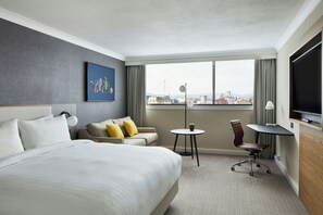 A hotel room with a large bed, a sofa, a small table, a chair, and a TV.
