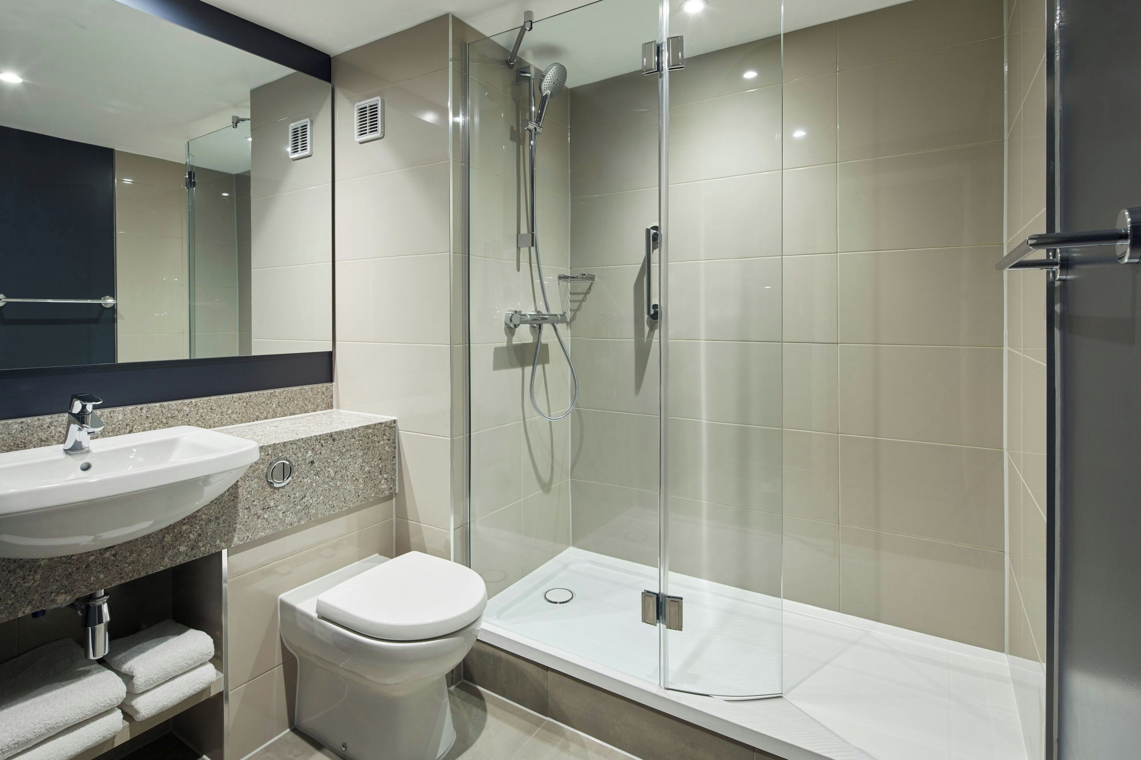 Un baño moderno con ducha envuelta en vidrio, lavamanos y retrete.