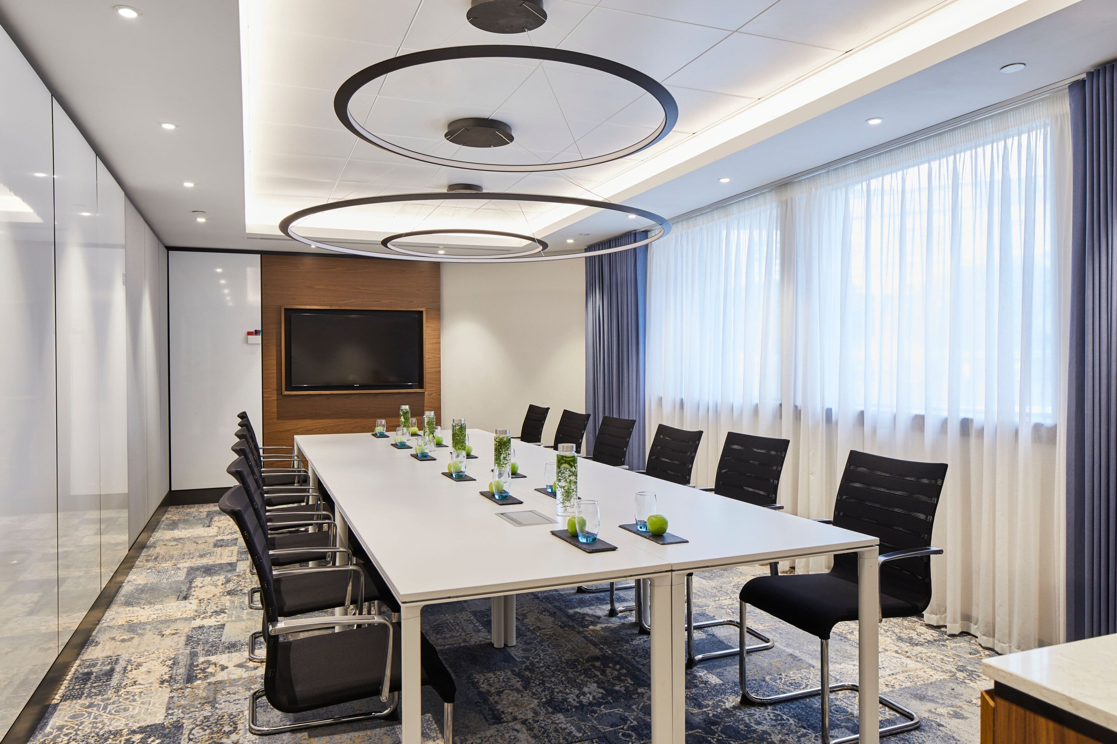 A conference room with a long table, chairs, and a TV screen.