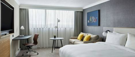 A hotel room with a bed, a desk, a chair, a sofa, and a television.