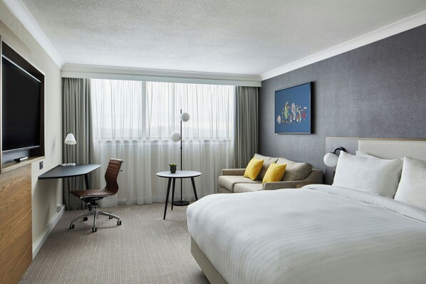 A hotel room with a bed, a desk, a chair, a sofa, and a television.