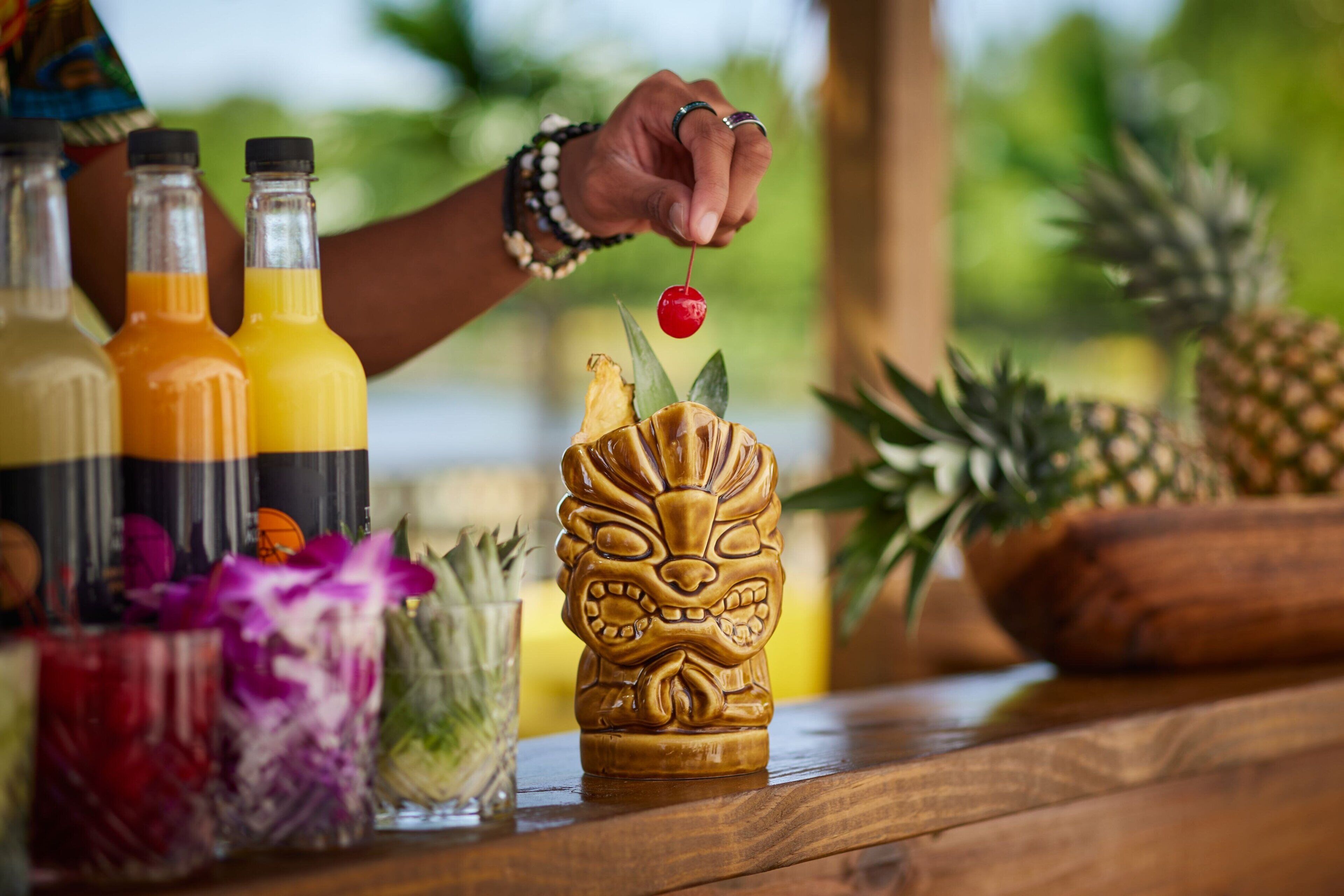 A wooden table with a carved wooden tiki head, a glass of juice, and bottles of orange juice.
