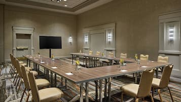 A conference room with a long table, multiple chairs, a flat-screen TV, and a carpeted floor.