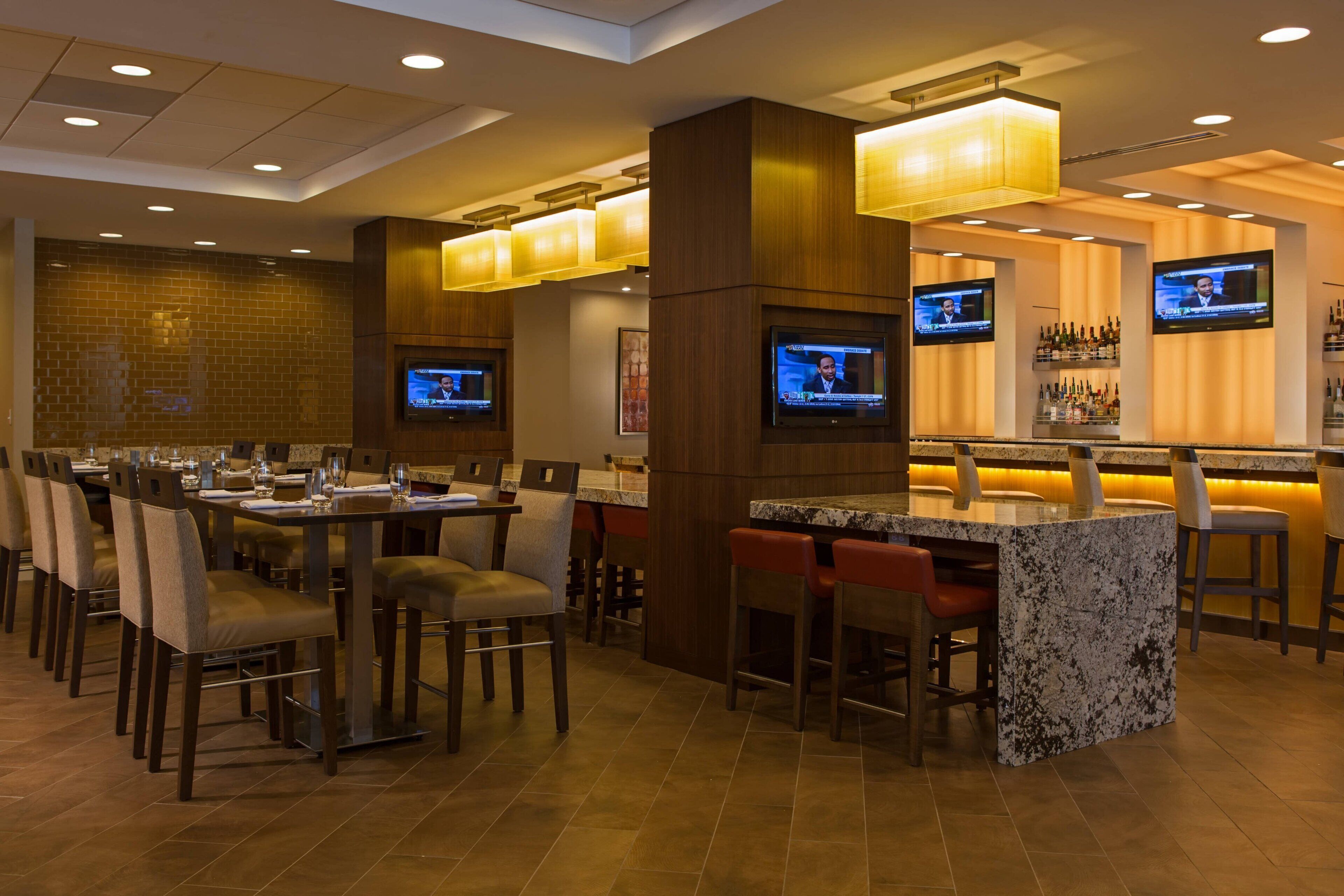 A hotel bar area with multiple seating arrangements, including a bar counter and several tables with chairs.