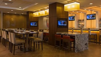 A hotel bar area with multiple seating arrangements, including a bar counter and several tables with chairs.