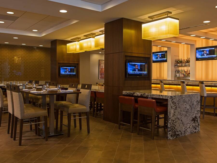 A hotel bar area with multiple seating arrangements, including a bar counter and several tables with chairs.