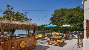 An outdoor seating area with wooden tables and chairs, a tiki bar, and umbrellas. - Gaithersburg Marriott Washingtonian Center (Gaithersburg)