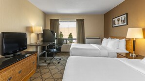 Une chambre d’hôtel avec deux lits, un bureau avec une télévision, une chaise et une fenêtre avec des rideaux.