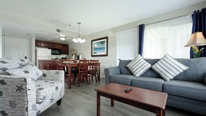 A living room with a grey sofa, striped pillows, a wooden coffee table, and a dining area with a wooden table and chairs. - Parc Corniche Condominium Suite Hotel (Orlando)