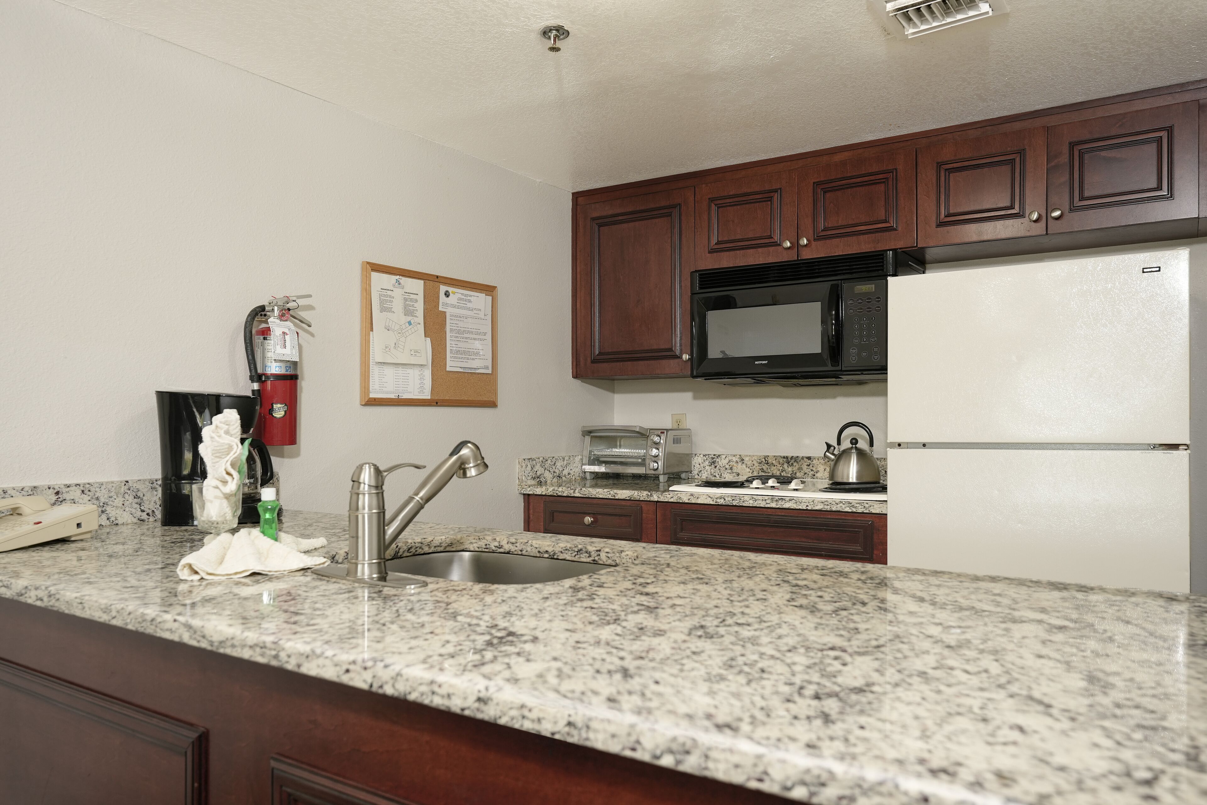 A kitchen with granite countertops, a stainless steel sink, a microwave, a toaster, and a refrigerator.