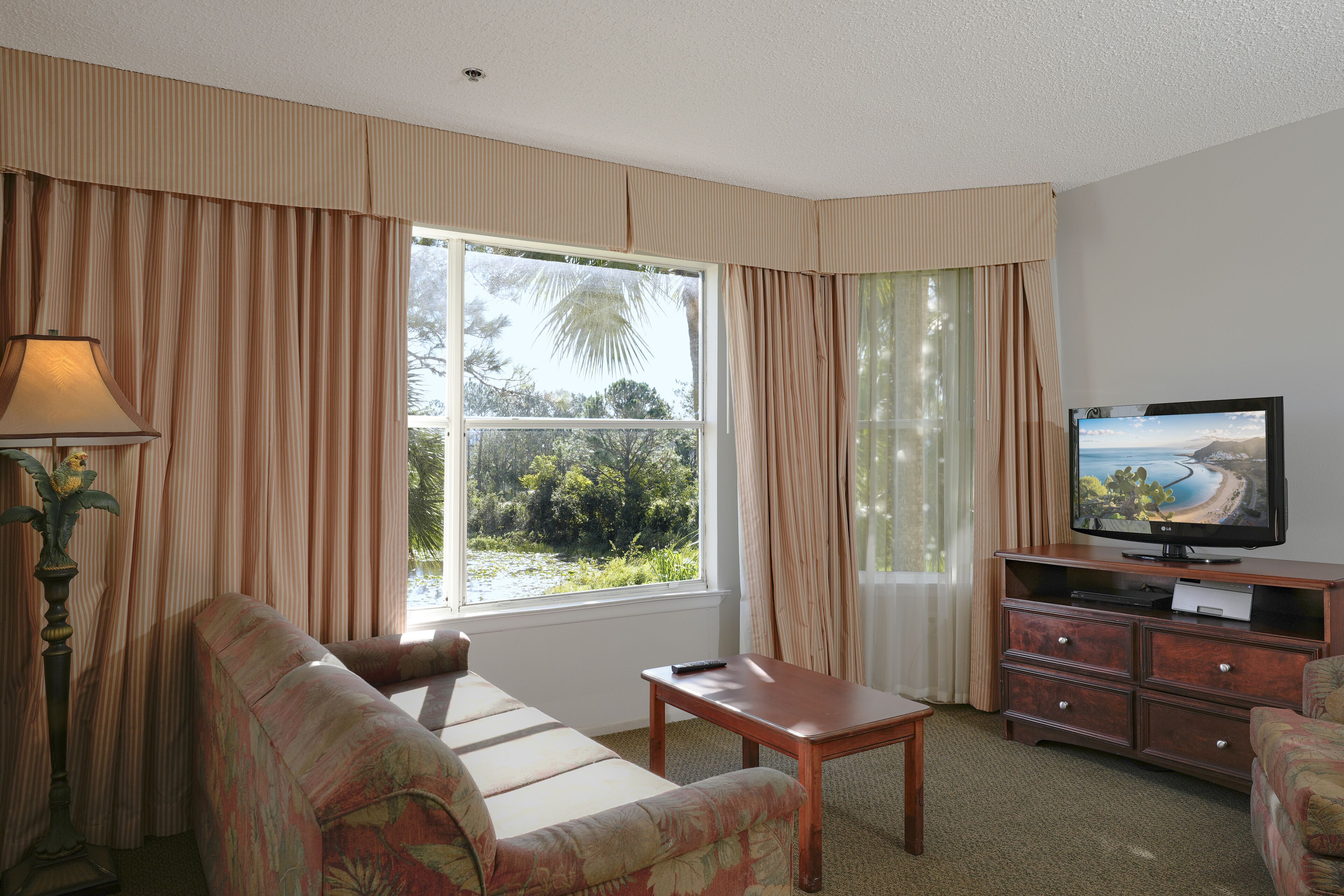 Una habitación con un sofá, un televisor sobre un mueble de madera, una lámpara y una ventana con cortinas.