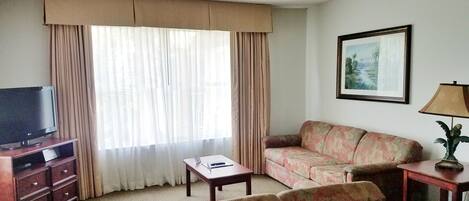 Una sala de estar con televisión, sofá, mesa de centro y lámpara.