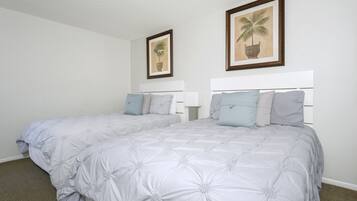 Een tweepersoonsbed met een wit hoofdeinde en een grijs beddegoed met bloemen. Boven het bed hangen twee ingelijste foto's aan de muur.