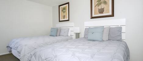 A double bed with a white headboard and a grey floral bedspread. There are two framed pictures on the wall above the bed.