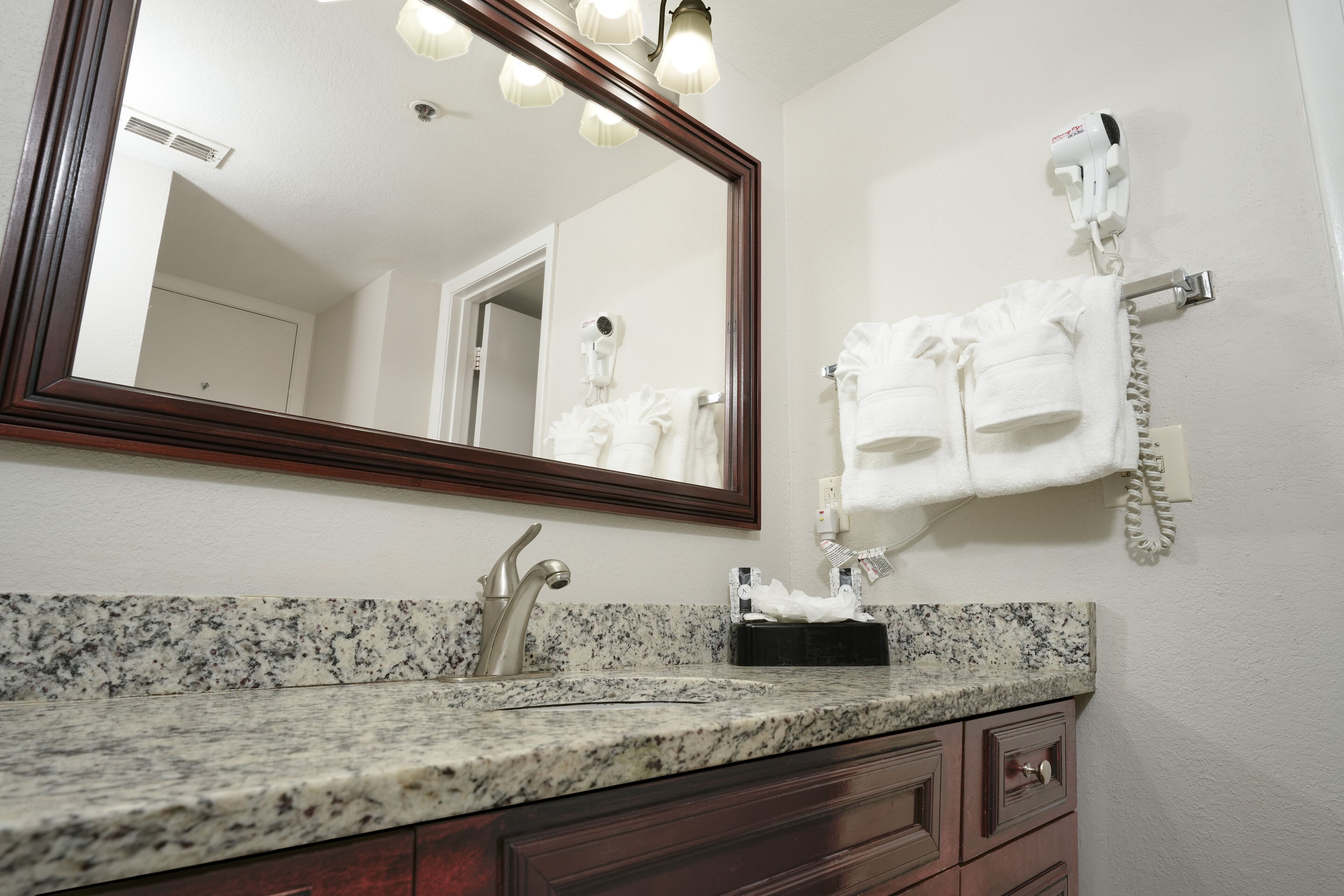 A bathroom with a granite countertop, a sink, a mirror, a towel rack, and a hairdryer.