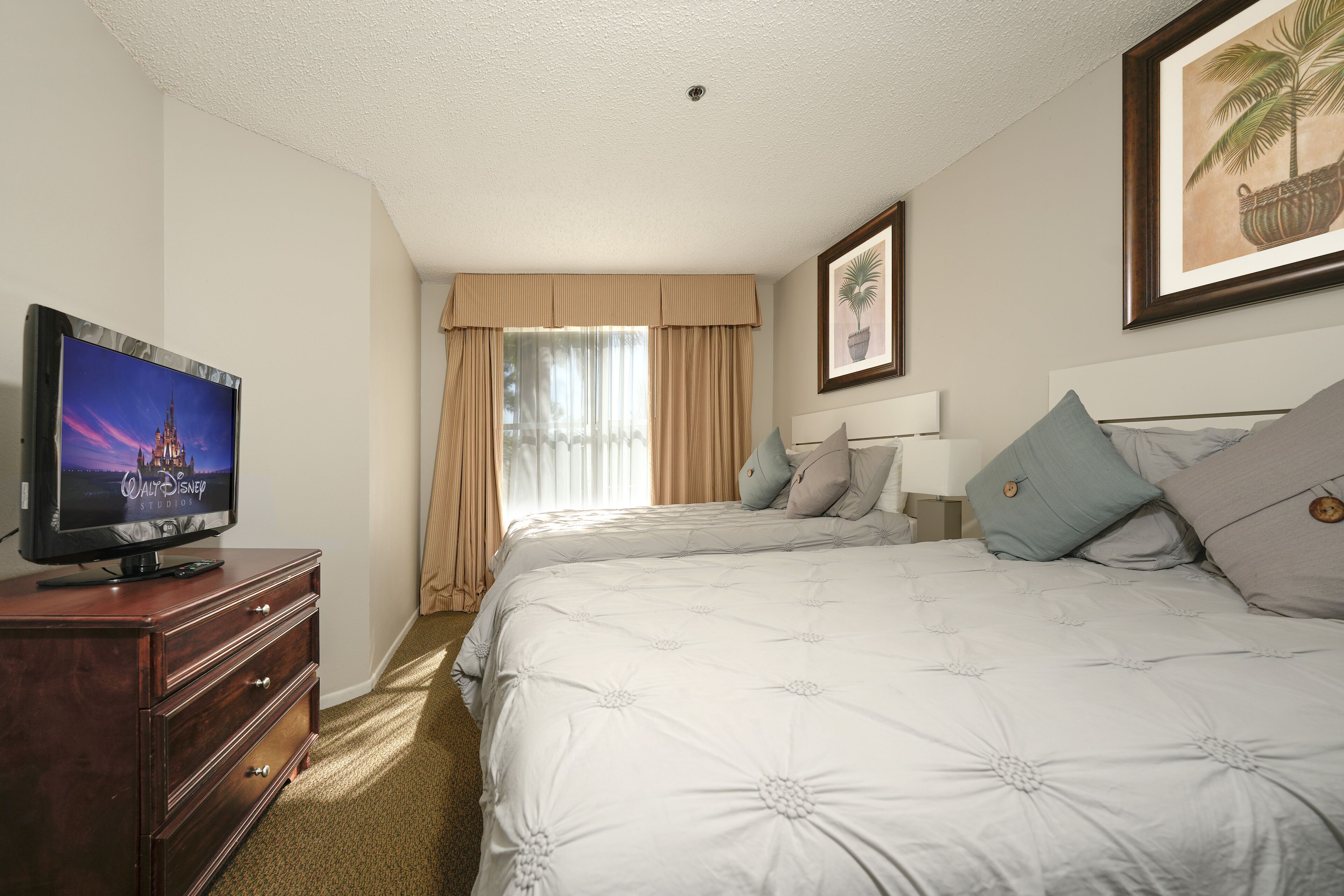 A hotel room with a large bed, a TV on a wooden dresser, a window with curtains, and a framed picture on the wall.