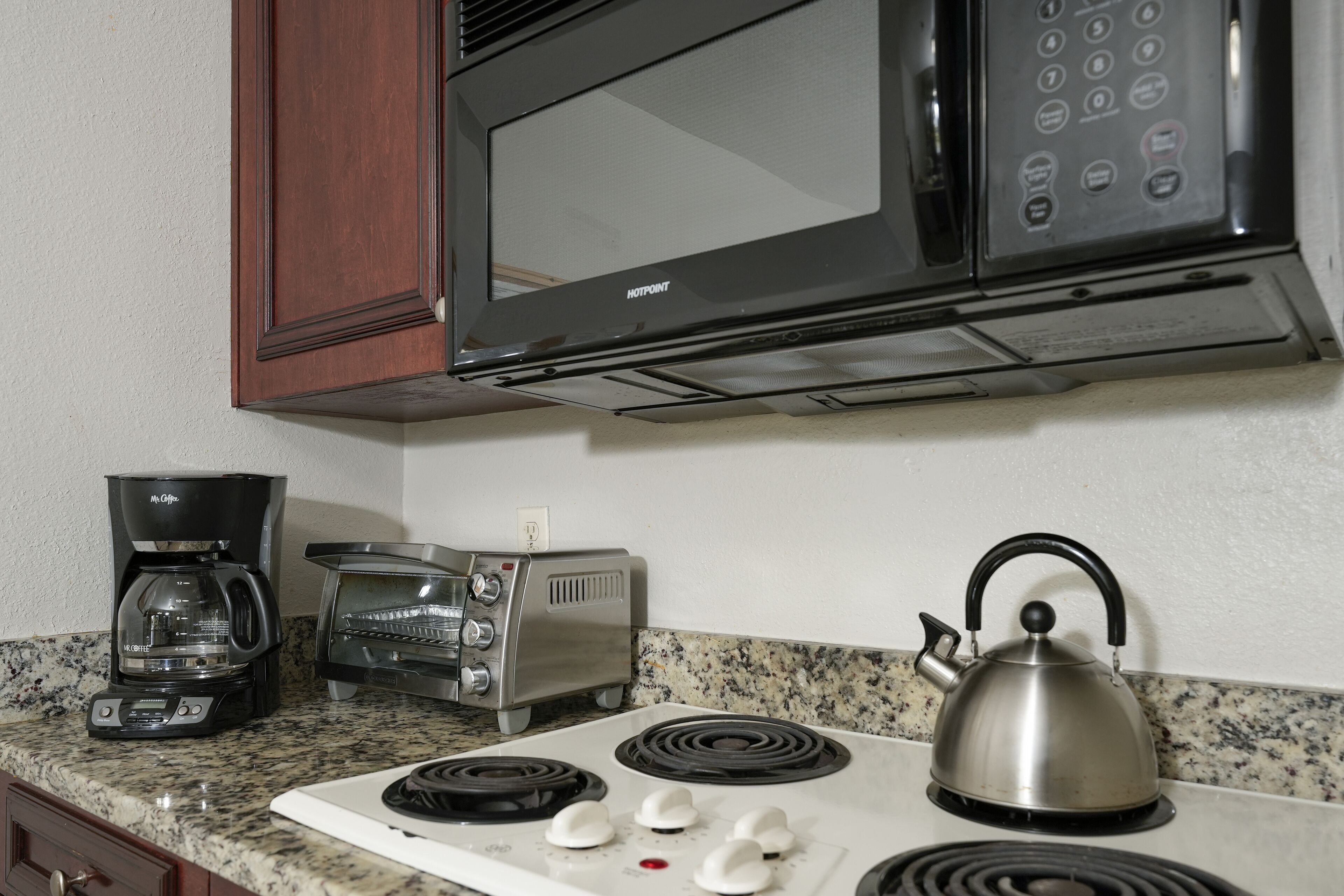 A kitchenette with a microwave, toaster, coffee maker, kettle, and stove.