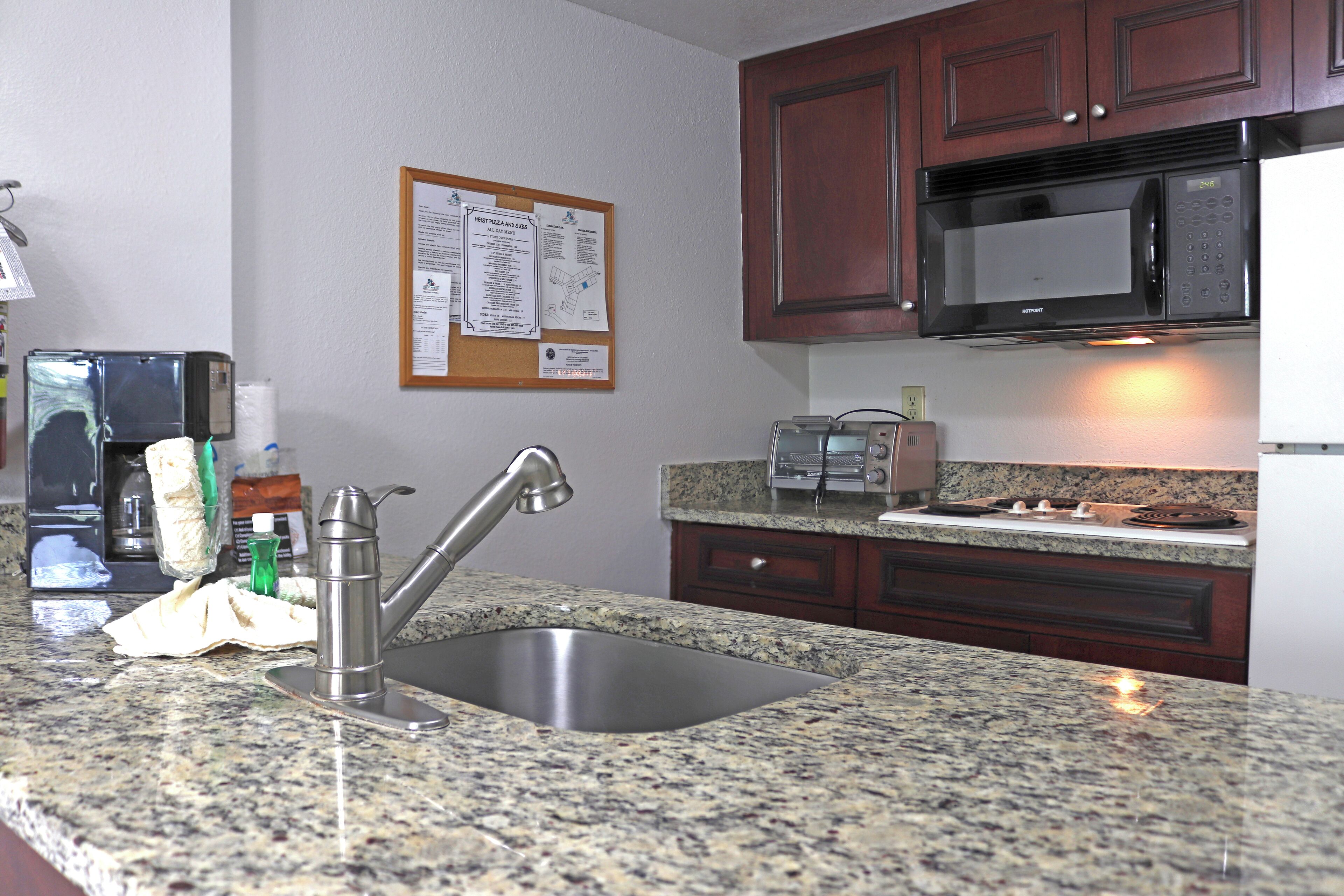 A kitchen with granite countertops, a stainless steel sink, a microwave, a toaster, and wooden cabinets.