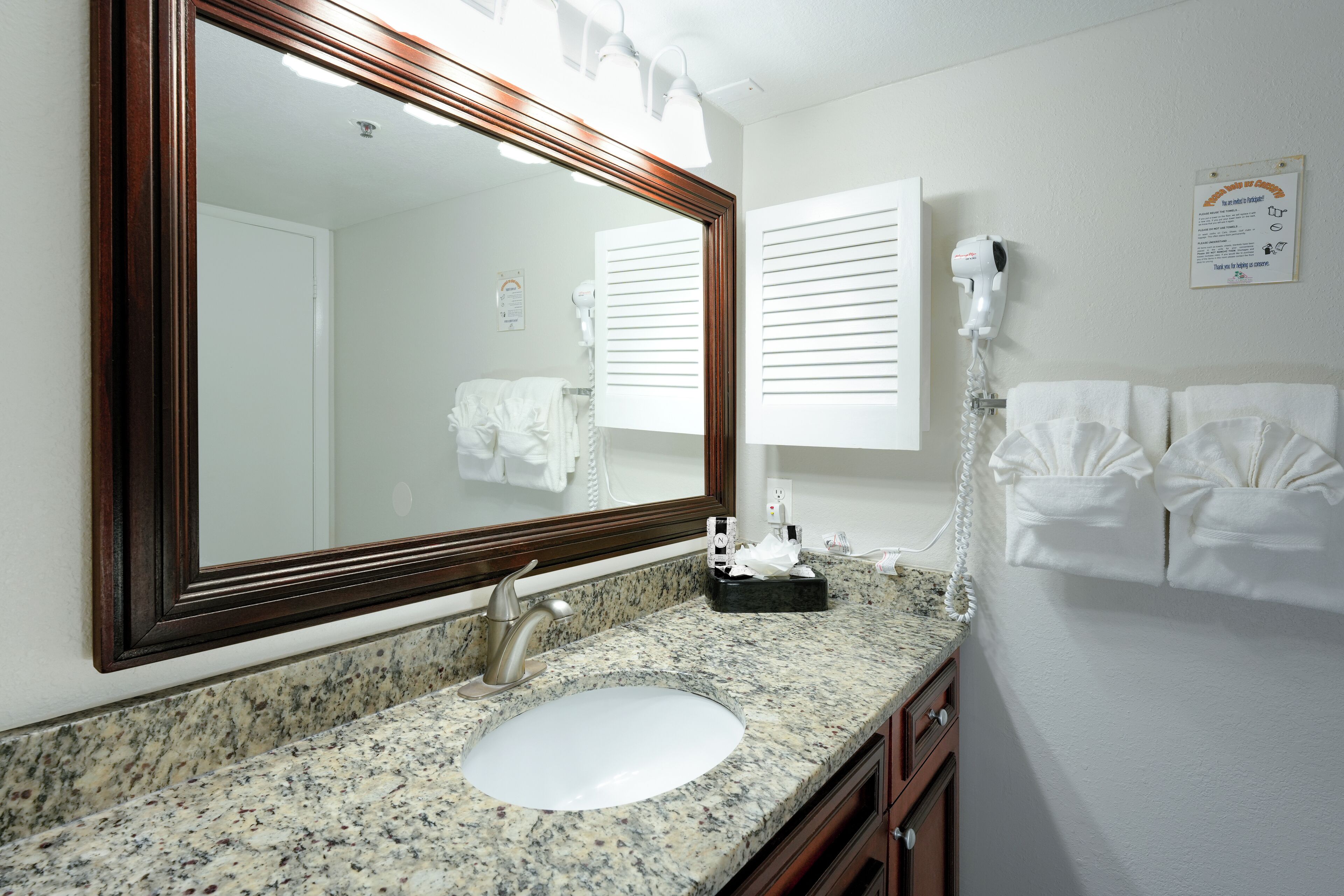 A bathroom with a granite countertop, a sink, a mirror, a hairdryer, and a towel rack.