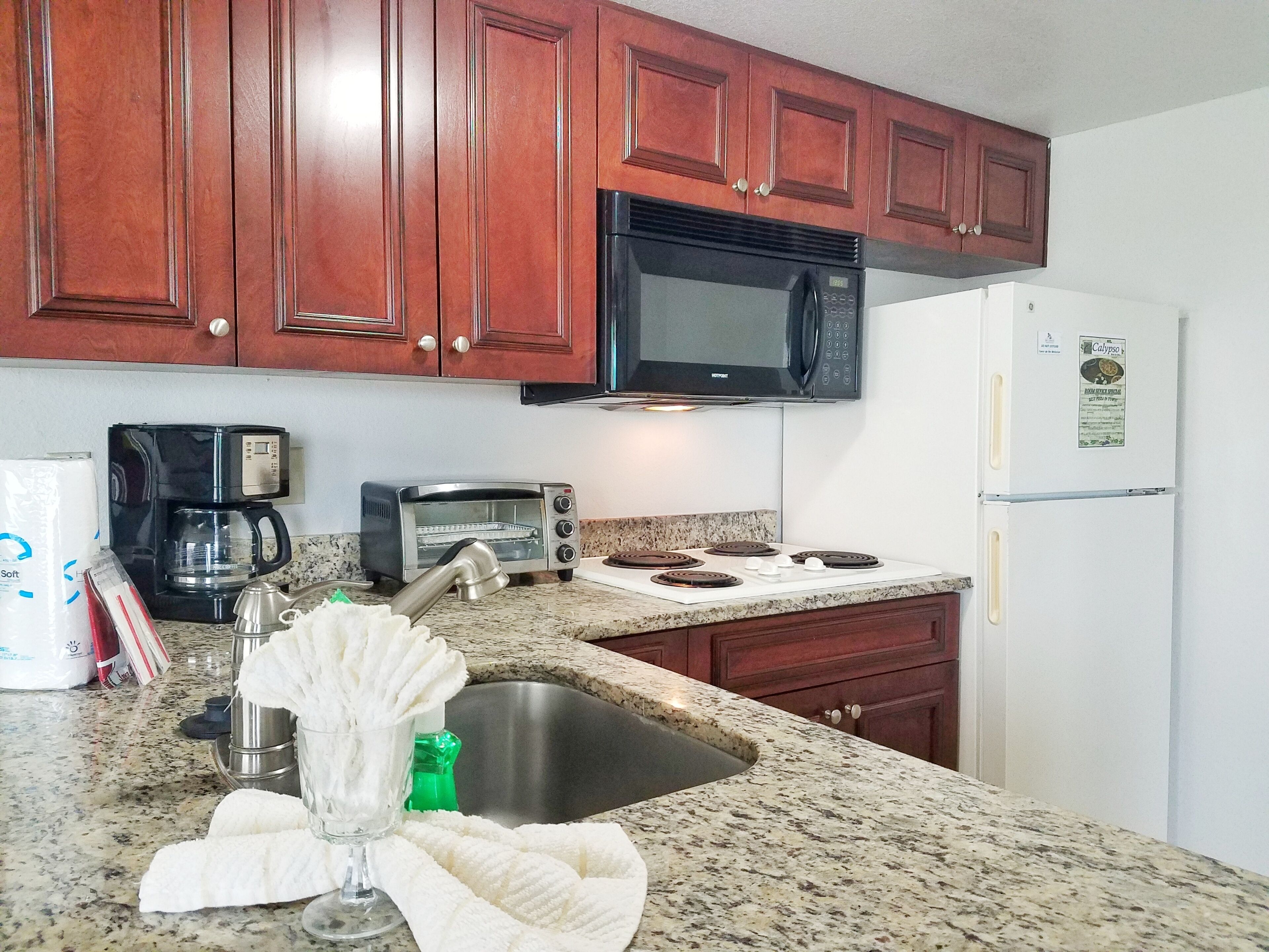 A kitchen with wooden cabinets, a microwave, a toaster, a coffee maker, a sink, and a refrigerator.