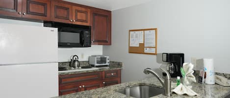 A kitchen with granite countertops, a stainless steel sink, wooden cabinets, a microwave, a toaster, and a coffee maker.
