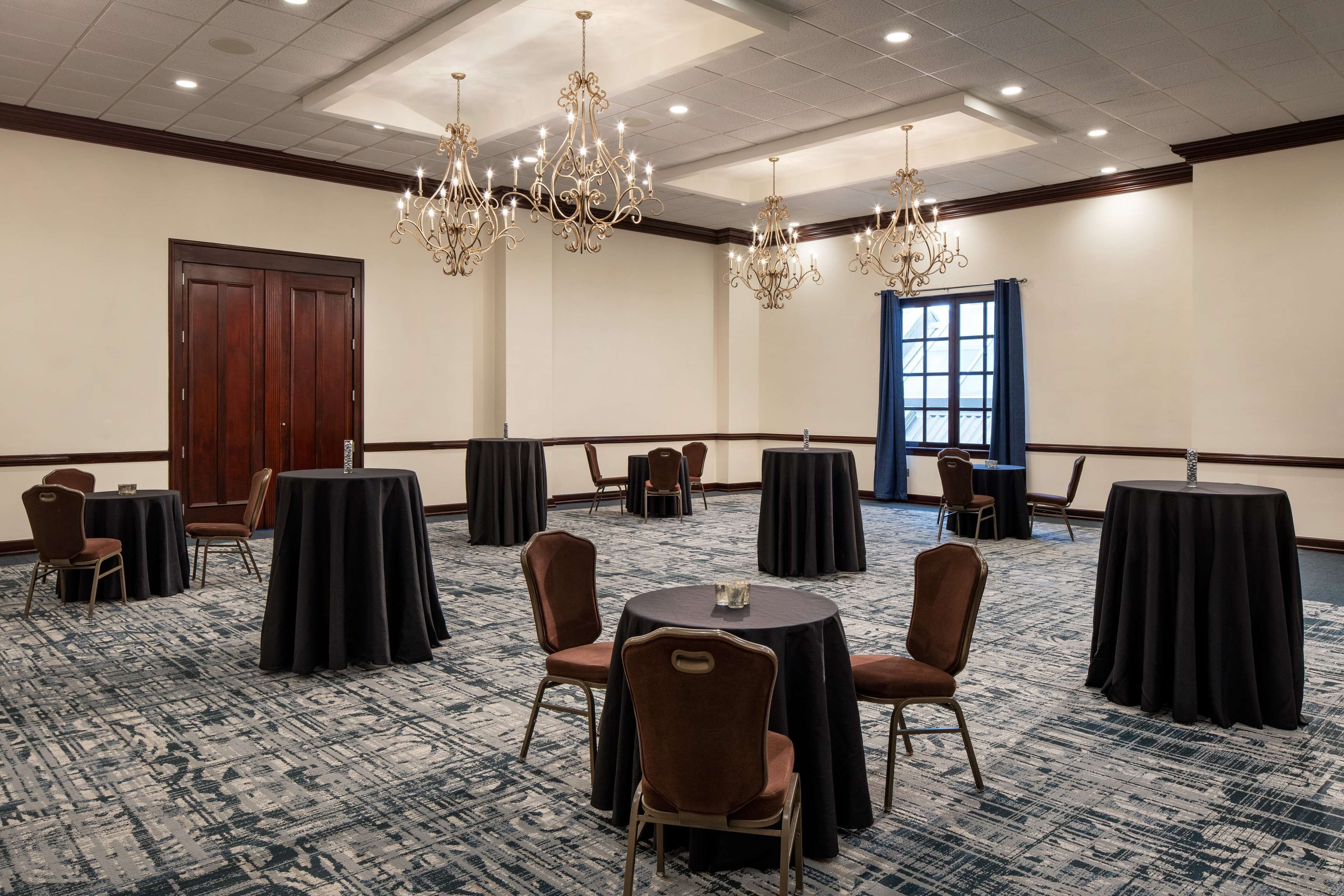 Un salón de conferencias con mesas redondas, sillas y candelabros.