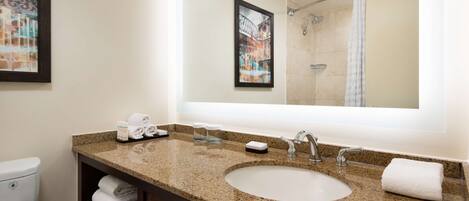 A bathroom with a granite countertop sink, a large mirror, and a shower visible in the reflection.