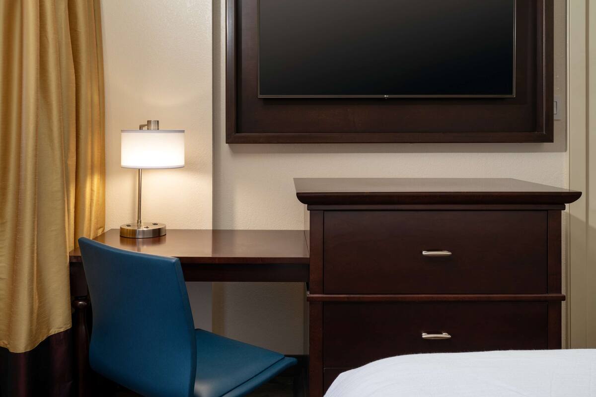 Een hotelkamer met een bed, een bureau met lamp, een stoel en een televisie die aan de muur is bevestigd.