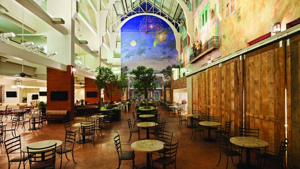 A spacious indoor atrium with multiple dining tables and chairs, a high ceiling with a mural, and a wooden wall on one side. - Embassy Suites by Hilton New Orleans (New Orleans)