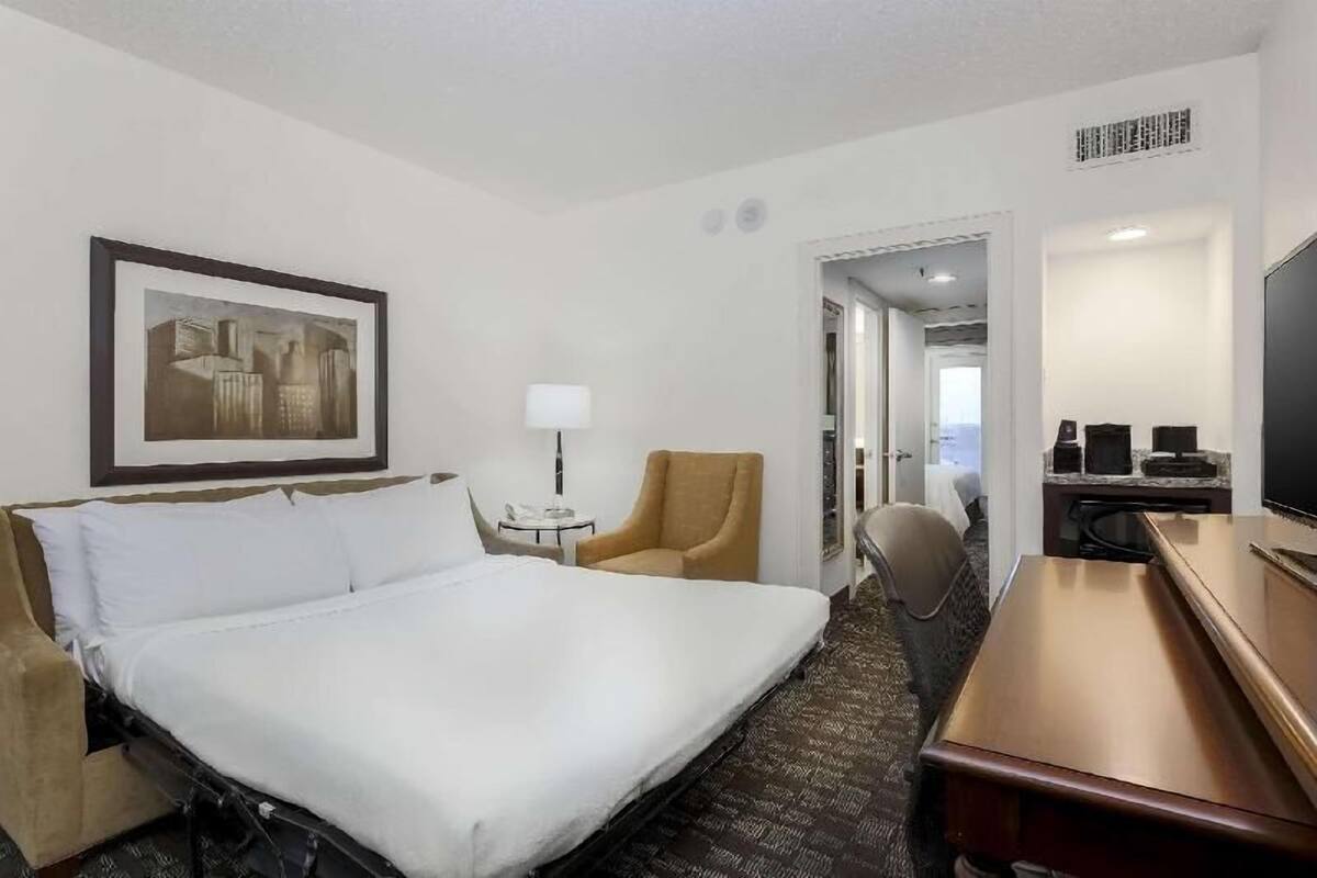 Een hotelkamer met een bed, een stoel, een bureau, een televisie en een lijst met een afbeelding aan de muur.